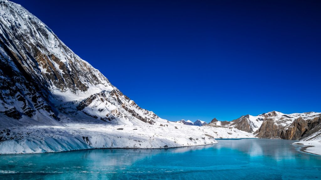 Bright blue glacial lake with snowy mountain peaks and golden larches